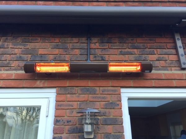 Tansun Bahama ultra low glare heater fitted to brick wall of house above windows and below an awning